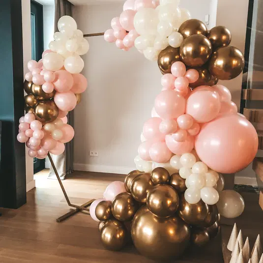 Dekoracja z balonów w kształcie łuku w pastelowych kolorach różu, złota i bieli na imprezę w eleganckim wnętrzu. 
