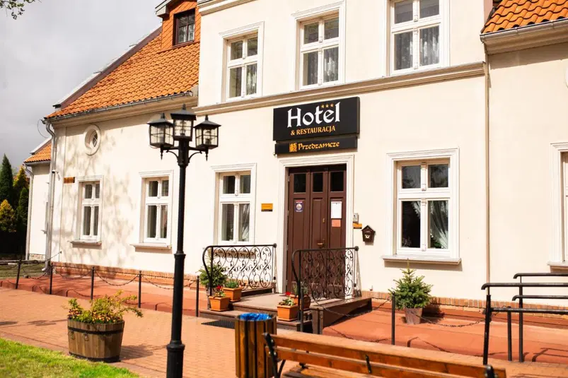  Hotel z restauracją Przedzamcze z klasycznym białym budynkiem i czerwoną dachówką, wejście z ozdobnymi donicami i latarnią. 
