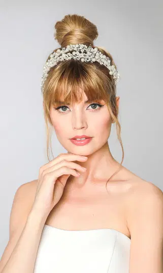  <p>Portret kobiety z blond włosami upiętymi w kok, ozdobnymi perłami we włosach, delikatny makijaż i elegancki strój na jasnym tle.</p> 