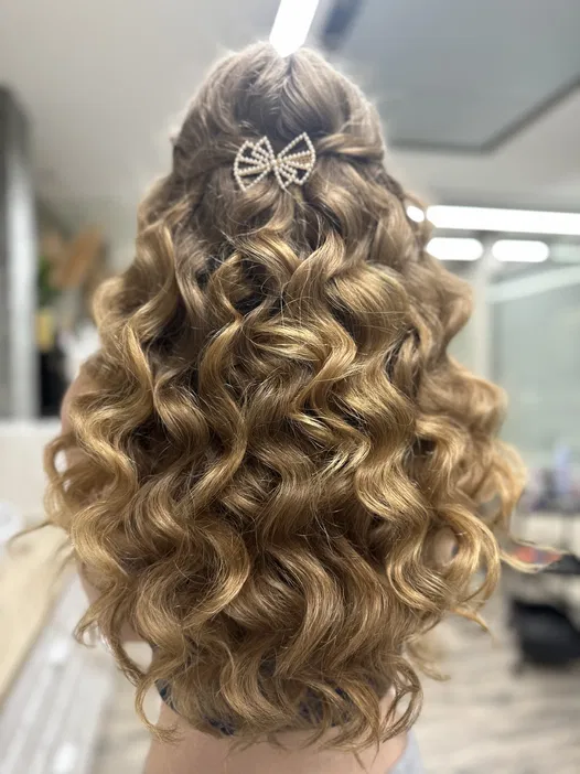 Lśniące, blond loki z biżuteryjną ozdobą w kształcie kokardy - elegancka fryzura na specjalne okazje w salonie fryzjerskim.