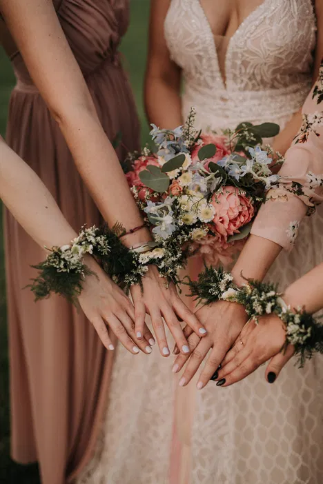 Bridesmaids and bride showing hands with floral bracelets and wedding bouquet.