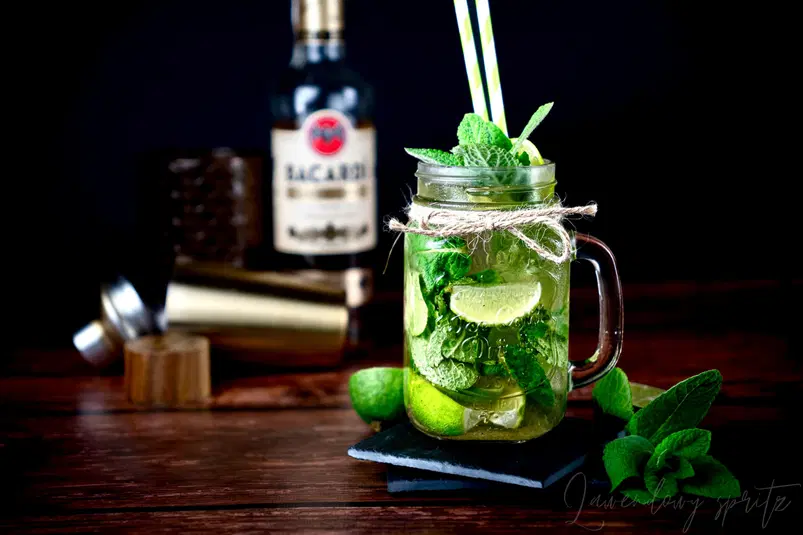  Koktajl mojito w słoiku z miętą i limonką na drewnianym stole, w tle butelka rumu i shaker. 