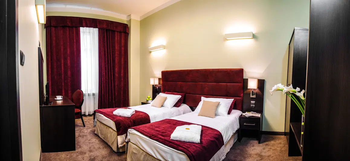  Dwuosobowy pokój hotelowy z wygodnymi łóżkami, eleganckim wystrojem i nastrojowym oświetleniem. Pełne wyposażenie, idealne na relaksujący pobyt. 