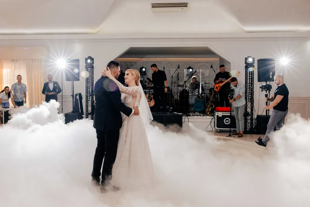 Pierwszy taniec pary młodej na weselu, romantyczny taniec w chmurach, orkiestra w tle, elegancka sala weselna.