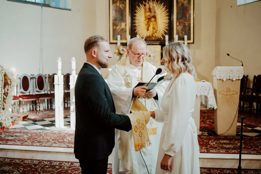 Ceremonia ślubna w kościele, para młoda wymienia przysięgi przed księdzem.