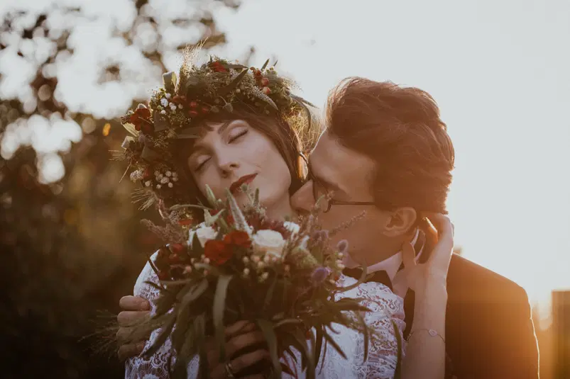  Ślubna sesja zdjęciowa o zachodzie słońca, para w romantycznym uścisku z kwiatową dekoracją i wiankiem na głowie, naturalne światło, ślub na świeżym powietrzu. 