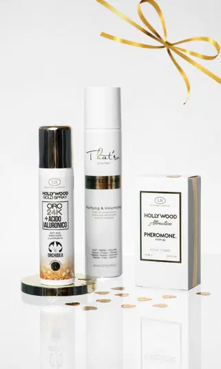  Kosmetyki do pielęgnacji skóry i włosów: serum z 24K złotem, spray do włosów i perfumy Hollywood Attraction na białym tle z ozdobną złotą wstążką. 