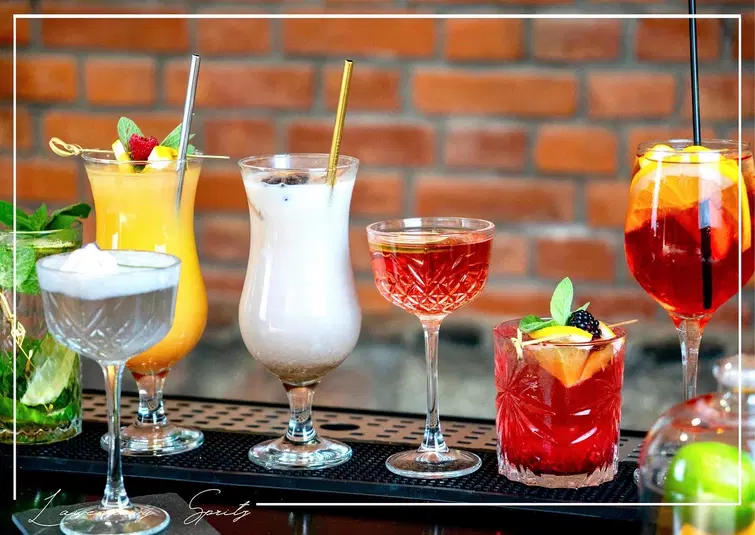  Różnorodne koktajle na tle ceglanej ściany, elegancko podane drinki w kolorowych szklankach, idealne na imprezę lub relaksujący wieczór. 