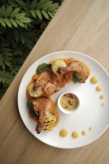  Elegancko podane danie gourmet z grillowanym kurczakiem, puree, grillowaną kukurydzą i sosem na białym talerzu, na drewnianym stole z liśćmi w tle. 