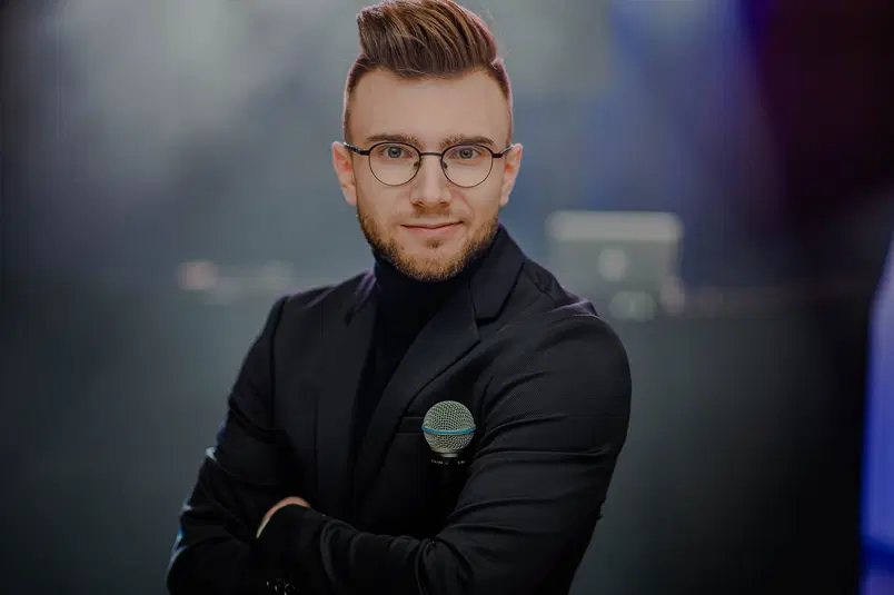  Mężczyzna w eleganckim garniturze z mikrofonem w dłoni, z uśmiechem na twarzy, w studio fotograficznym. 