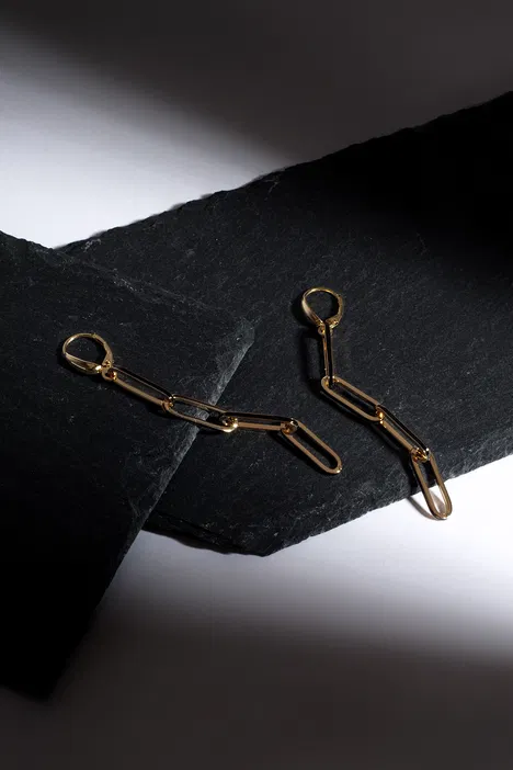 Złote kolczyki na tle czarnego kamienia, elegancka biżuteria, minimalistyczny design.