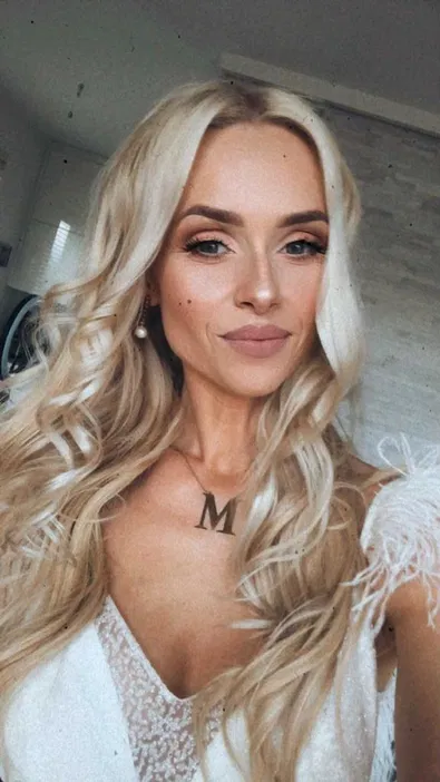 Nie wiem, kto to jest na zdjęciu. Młoda, długowłosa kobieta z blond włosami, nosząca elegancki strój i naszyjnik z literą M.