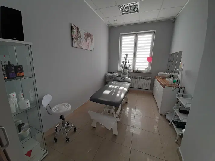  Gabinet kosmetyczny z łóżkiem do masażu, krzesłem obrotowym i kosmetykami na półce. 