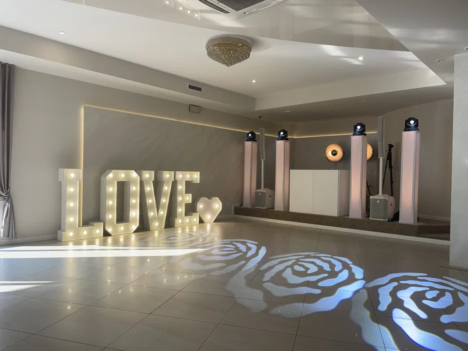 Dekoracja weselna w postaci dużych, podświetlanych liter LOVE na eleganckim parkiecie w nowoczesnej sali bankietowej.