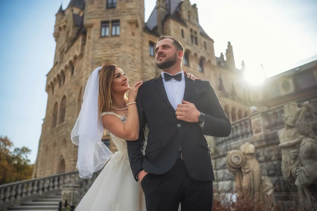 Para młoda przed zabytkowym zamkiem w słoneczny dzień, ślubna sesja fotograficzna na tle architektury.