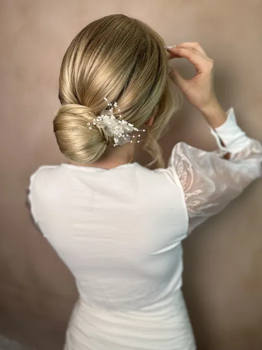 Blond włosy upięte w elegancki kok z ozdobą z pereł, kobieta w białej sukience, widok od tyłu.