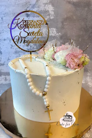 Tort na Pierwszą Komunię Świętą z delikatną dekoracją z kwiatów i różańcem na wierzchu, złoty topper z imieniem Magdalena, elegancki tort komunijny na złotej podstawce.