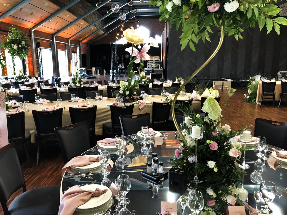 Elegancka sala weselna z nowoczesnymi dekoracjami kwiatowymi, okrągłe stoły przygotowane na przyjęcie, stylowe nakrycia i delikatne oświetlenie, idealne miejsce na organizację luksusowego wesela.