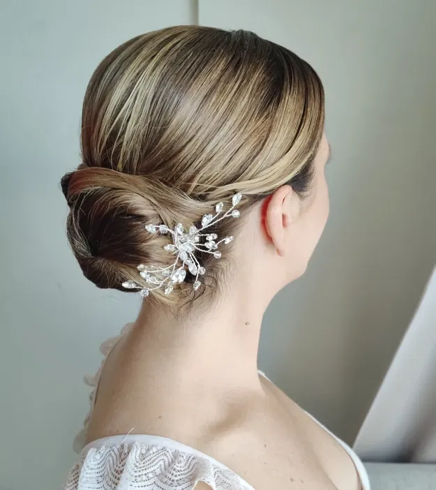 Upięcie ślubne z ozdobną spinką z kryształkami na blond włosach.