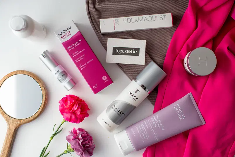  Produkty kosmetyczne sesderma, Dermaquest, Image Skincare, Paulas Choice na tle różowej tkaniny z lustrem i kwiatami. 
