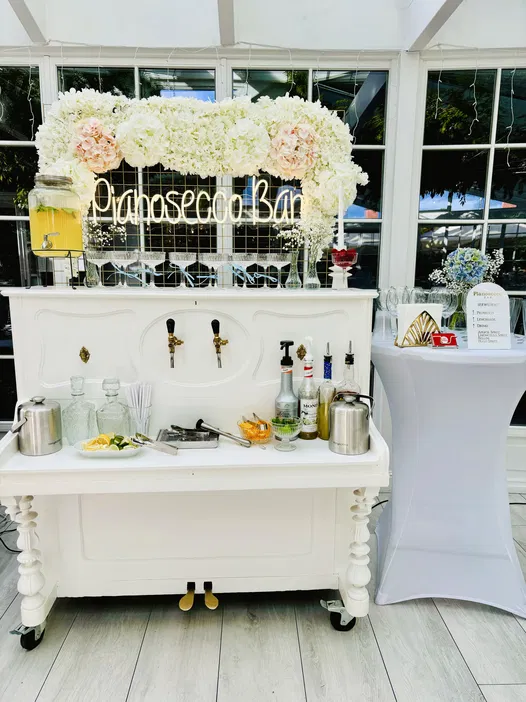Stylowy bar Prosecco z dekoracjami kwiatowymi, akcesoriami do drinków i napojami w szklanych butelkach podczas eleganckiego przyjęcia.
