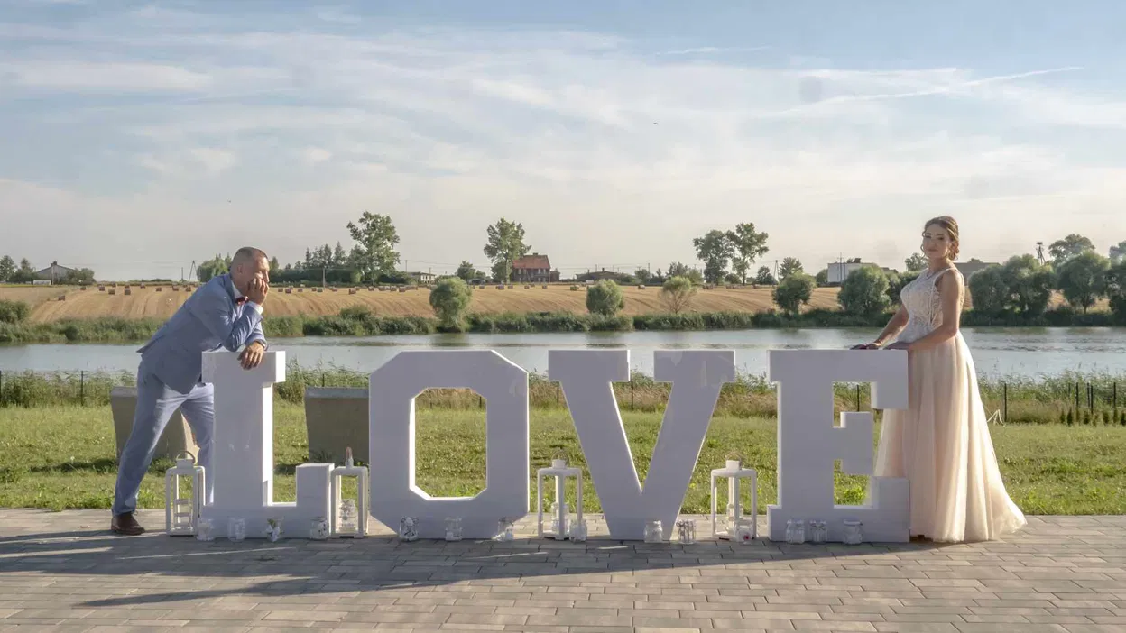 Para w eleganckich strojach przy dużych literach LOVE nad jeziorem, romantyczna sceneria weselna.
