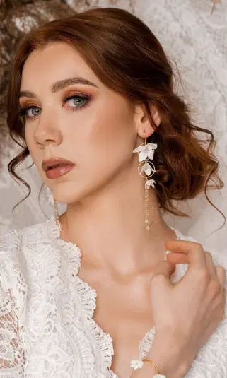  Kobieta w białej koronkowej sukience z eleganckimi kwiatowymi kolczykami i subtelnym makijażem, zbliżenie twarzy. 