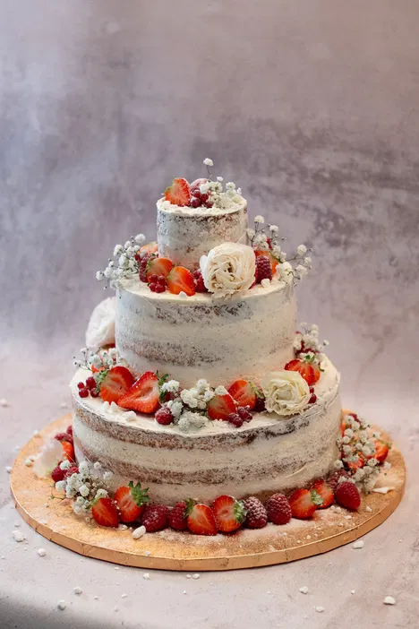 Tort weselny z owocami, truskawkami i kwiatami na trzech poziomach, w stylu naked cake, elegancka dekoracja.