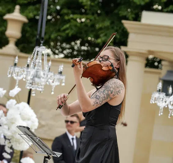  Skrzypaczka występująca na zewnątrz, elegancka sceneria z żyrandolami w tle, koncert w plenerze. 