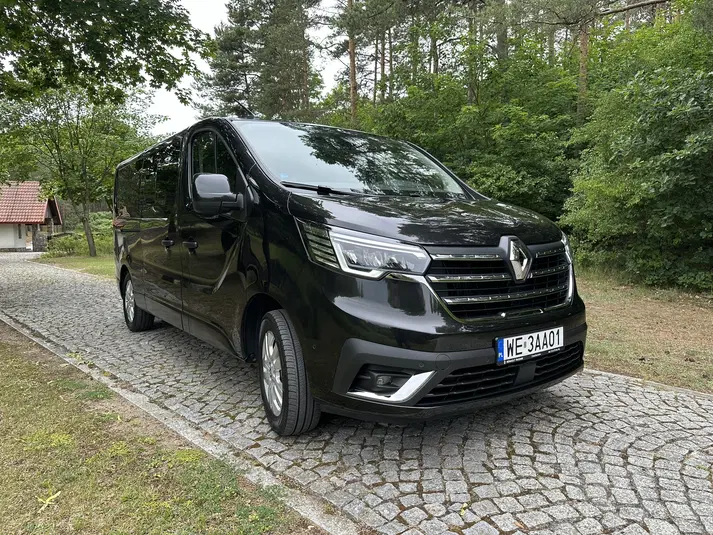  Czarny van Renault zaparkowany na brukowanej drodze, otoczony przez drzewa. 
