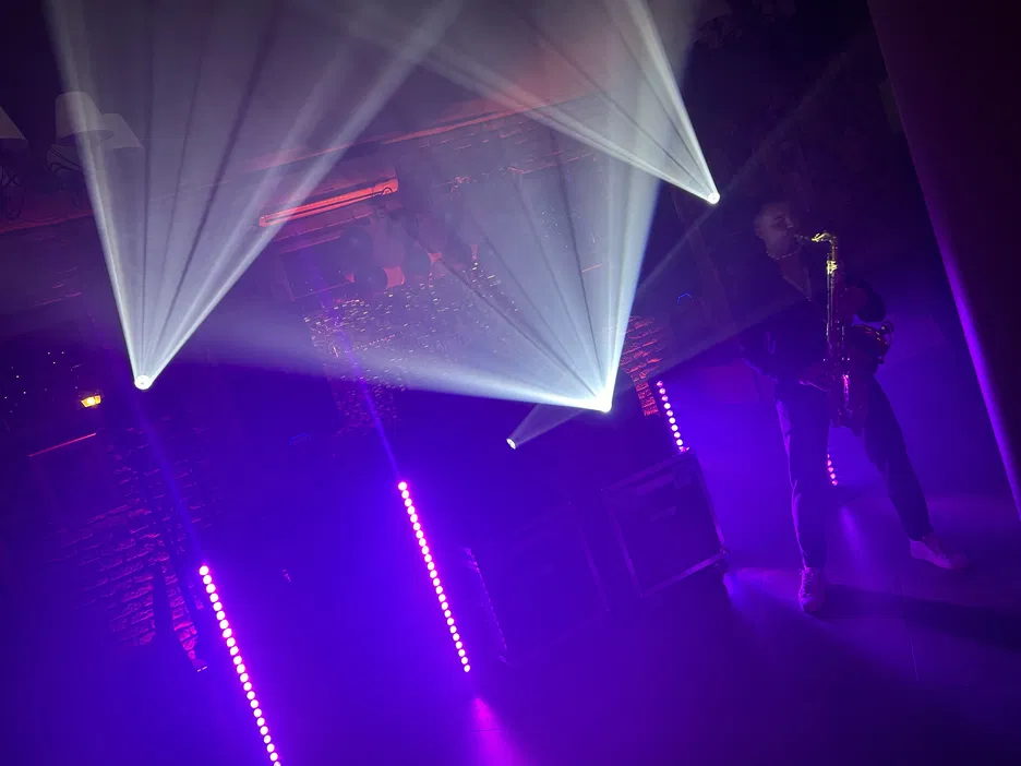 Muzyk grający na saksofonie na scenie z efektownym oświetleniem i laserowymi światłami. Atmosfera koncertu, fioletowe reflektory, muzyka na żywo.
