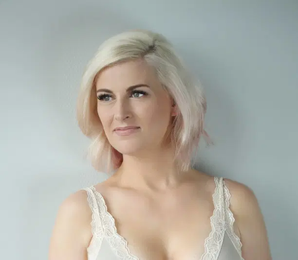  Portret młodej kobiety z blond włosami, w koronkowej bluzce na jasnym tle 