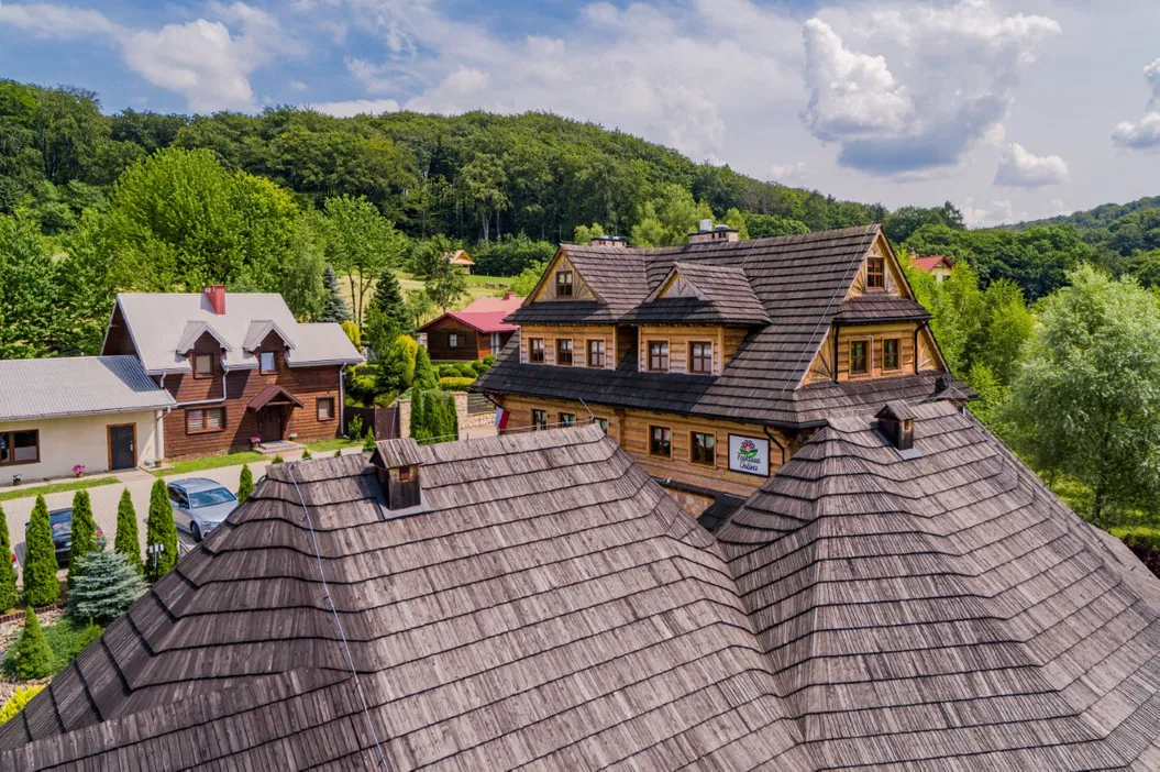 Drewniany pensjonat w malowniczej okolicy górskiej, otoczony zielenią i lasem, z tradycyjną architekturą i nowoczesnymi udogodnieniami.