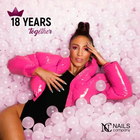  Kobieta w różowej kurtce puchowej w otoczeniu białych balonów, świętująca 18-lecie Nails Company. 