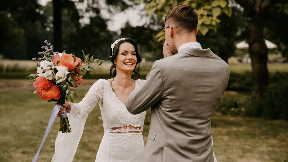  Panna młoda i pan młody podczas ceremonii ślubnej na świeżym powietrzu, kobieta w białej sukni ślubnej trzyma bukiet kolorowych kwiatów. 