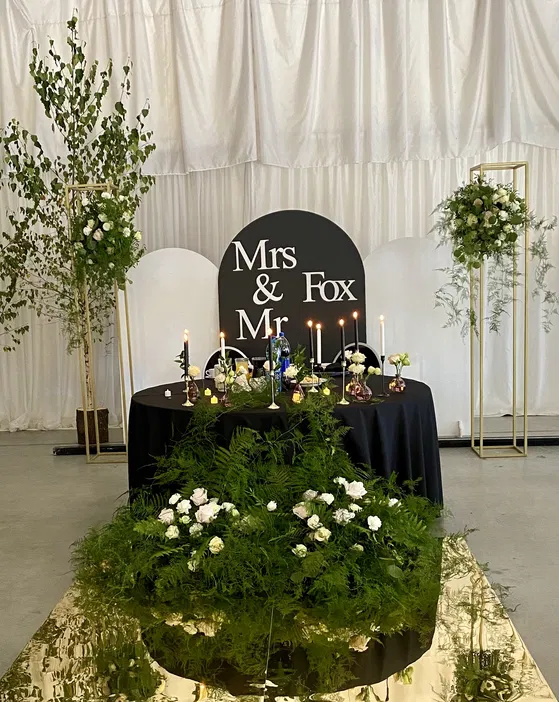 Dekoracja stołu weselnego z eleganckimi kompozycjami kwiatowymi i świecami, tło z napisem Mr & Mrs Fox.