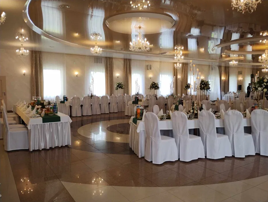 Luksusowa sala weselna z eleganckimi dekoracjami i kryształowymi żyrandolami, przygotowana na przyjęcie weselne.