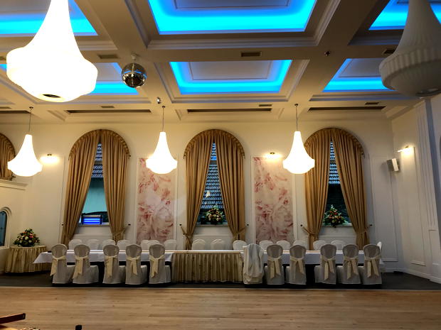 Elegancka sala bankietowa z białymi krzesłami, złotymi zasłonami i nastrojowym oświetleniem sufitowym, idealna na wesele lub konferencję. 