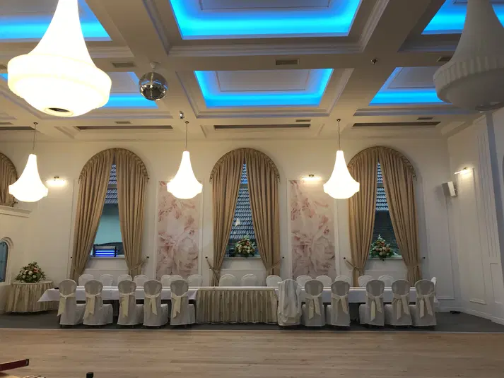  Elegancka sala bankietowa z białymi krzesłami, złotymi zasłonami i nastrojowym oświetleniem sufitowym, idealna na wesele lub konferencję. 