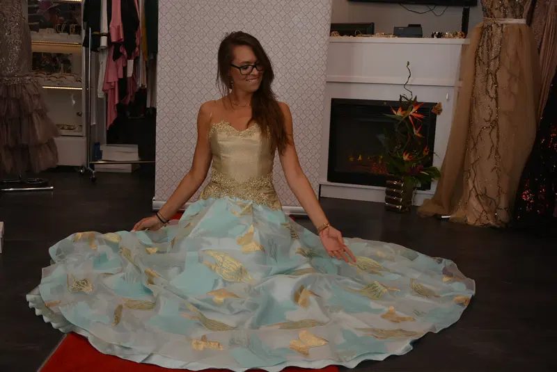  Osoba w eleganckiej sukni balowej z motywem motyli siedzi na podłodze w salonie mody, otoczona sukniami wieczorowymi. 