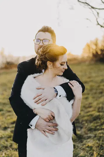  Para młoda w eleganckich strojach podczas romantycznej sesji ślubnej na tle zachodzącego słońca w plenerze. 