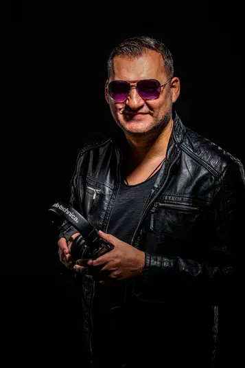  Mężczyzna w skórzanej kurtce i okularach przeciwsłonecznych trzyma słuchawki Audio-Technica, ciemne tło. 