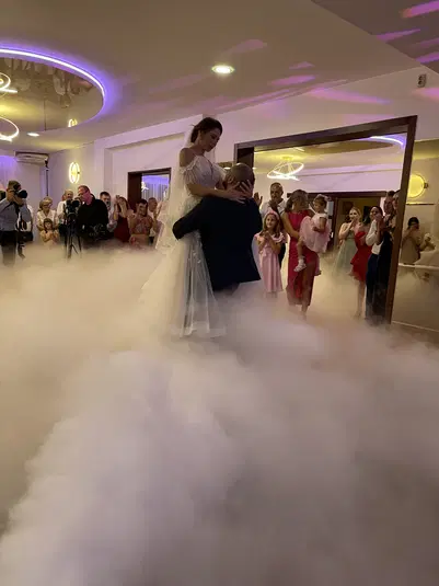  Para młoda na parkiecie podczas pierwszego tańca w otoczeniu gości weselnych, z efektem dymu i kolorowym oświetleniem, sala weselna, eleganckie wesele. 