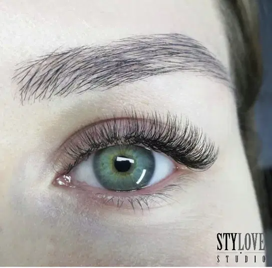  Zbliżenie na oko z zieloną tęczówką i długimi, gęstymi rzęsami, stylizacja brwi, profesjonalny makijaż oka, Stylove Studio. 