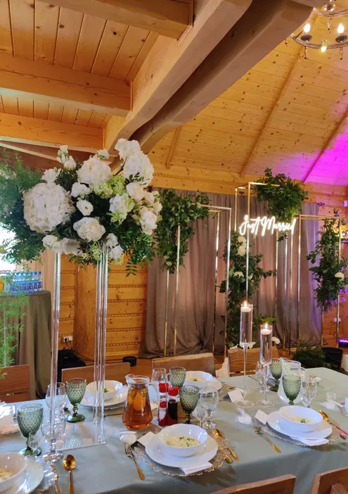 Stoły weselne z dekoracjami kwiatowymi w drewnianej sali, elegancka dekoracja, naczynia i sztućce na stole, styl rustykalny, napis Just Married na tle.