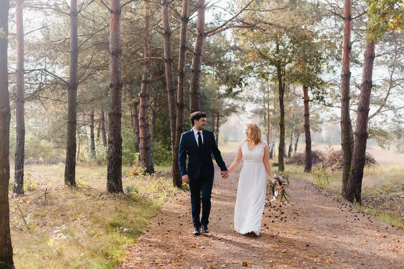  Para młoda spacerująca po lesie w promieniach słońca, elegancki garnitur i suknia ślubna, romantyczna sesja zdjęciowa na świeżym powietrzu. 