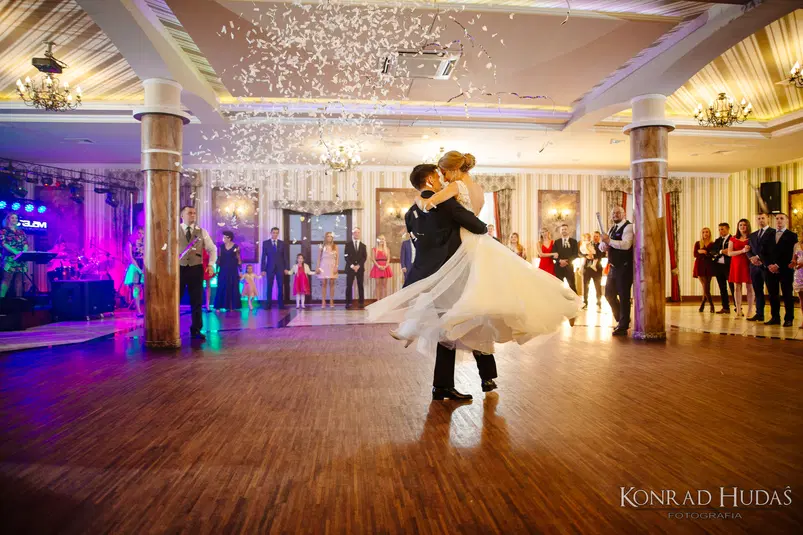  Para młoda tańcząca pierwszy taniec na eleganckim weselu, otoczona gośćmi weselnymi i dekoracjami, konfetti w powietrzu. 