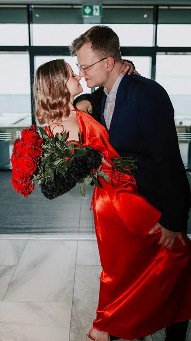 Para w eleganckich strojach z bukietem czerwonych róż, romantyczny moment w jasnym wnętrzu.