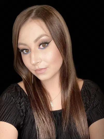  User with long brown hair and dramatic makeup against a black background. 