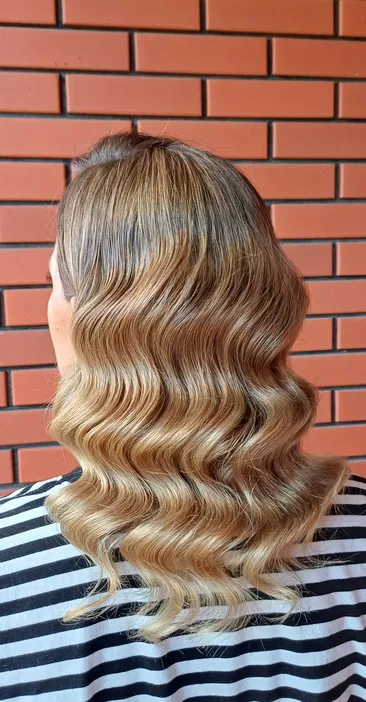 Fale blond na długich włosach, naturalny efekt, ceglana ściana w tle.
